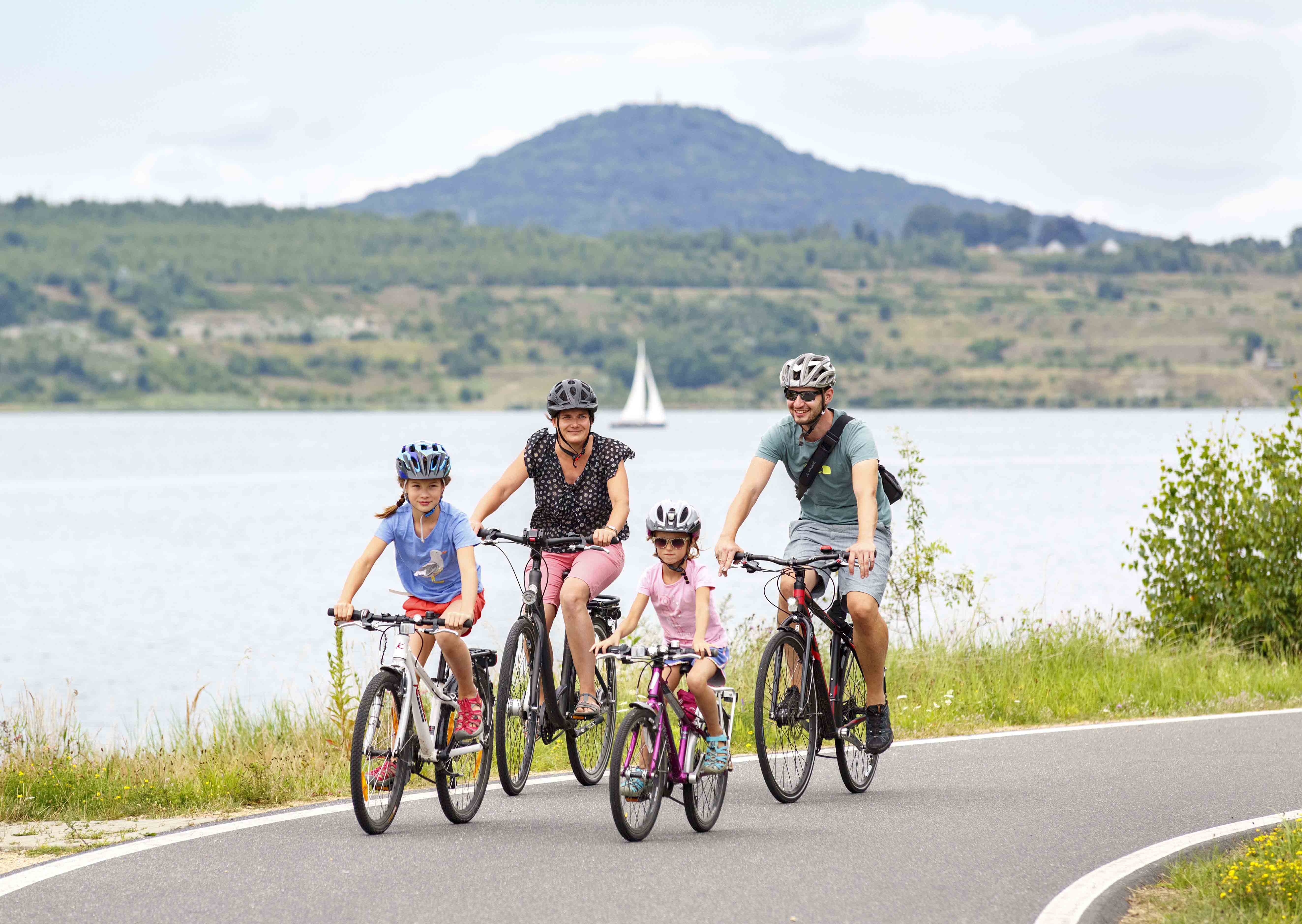 Eine Familie mit zwei Kindern fährt bei schönem Wetter auf dem See-Radweg